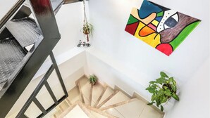 A modern staircase with a metal railing, a wall-mounted abstract painting, and potted plants. - Airy Penthouse with Private Rooftop Terrace in a Quaint Colombian Neighbourhood (Envigado)