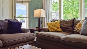 A living room with two brown sofas, a wooden coffee table, a lamp, and a view of the outdoors through a window. - Spacious 4 Bed, Central AC, Fire Pit, Grill, Games (Colorado Springs)