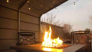 An outdoor patio with a fire feature, two chairs with patterned cushions, and a string of lights. - Spacious 4 Bed, Central AC, Fire Pit, Grill, Games (Colorado Springs)