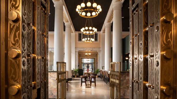 A grand lobby with ornate doors, a chandelier, marble flooring, and a central seating area. - The Liberty Trust (Roanoke)