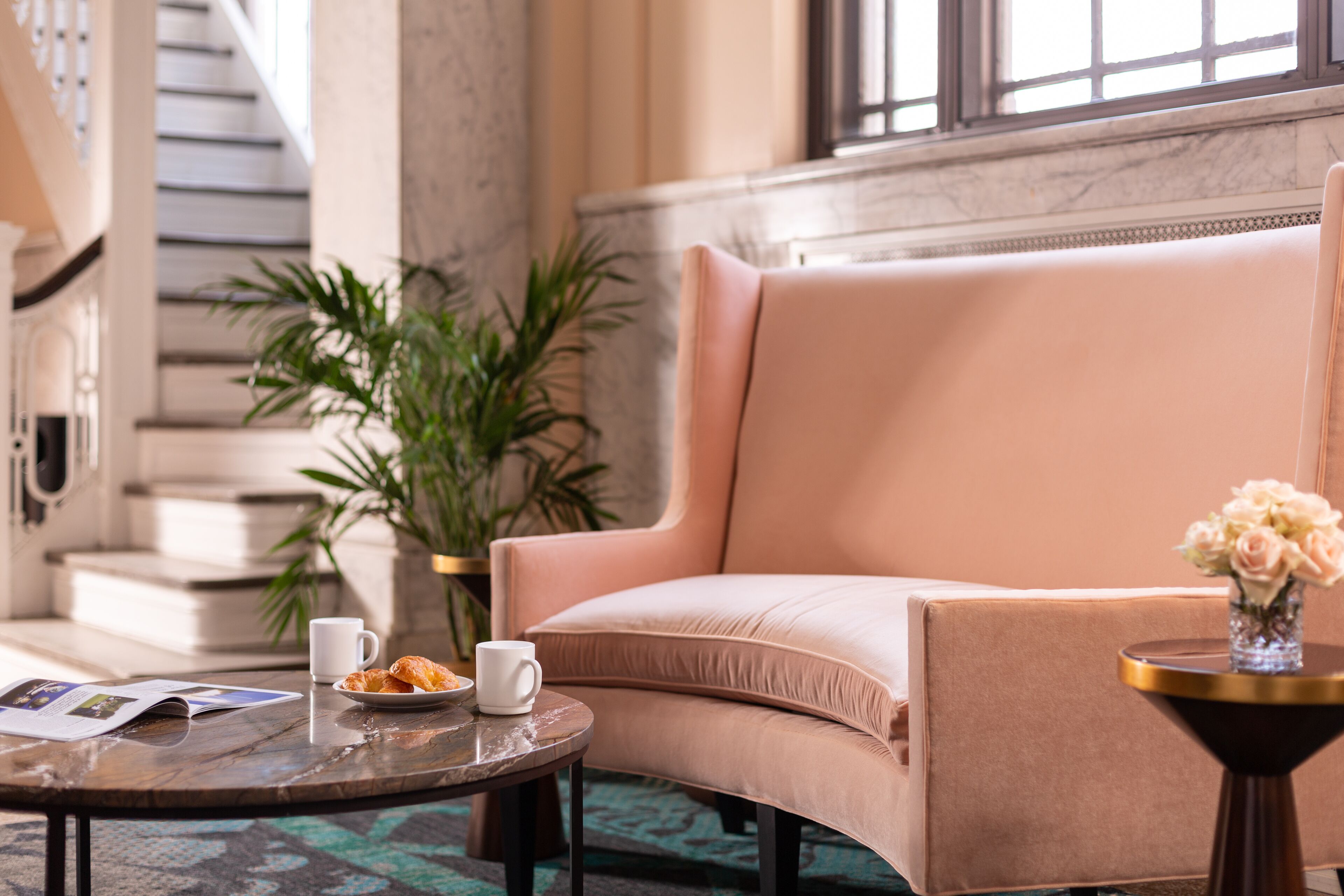 Un espace de détente moderne avec un canapé moelleux, une table basse sur laquelle sont disposées des pâtisseries, un vase rempli de fleurs et un escalier en arrière-plan.