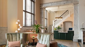 A spacious lobby with two plush armchairs, a reception desk, a staircase, and a chandelier. - The Liberty Trust (Roanoke)