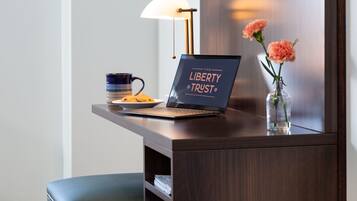 Un ordinateur portable posé sur un bureau, avec une pancarte indiquant « The Liberty Trust », une tasse, une assiette de biscuits et un vase rempli de fleurs.