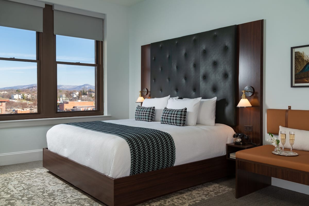 Habitación de hotel con una cama grande, una mesita de noche, una ventana con vistas a la ciudad y una lámpara de pared.