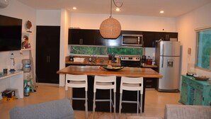 Una cocina moderna con una isla central, taburetes de bar, una lámpara colgante y un refrigerador.