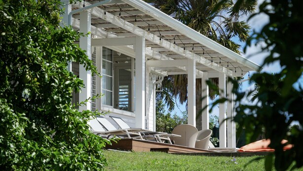 A covered outdoor seating area with a white pergola, a lounge chair, and a table.