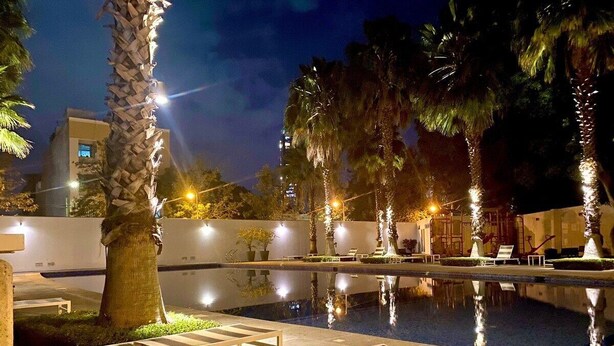 Zona de piscina nocturna con sillones de descanso y palmeras.
