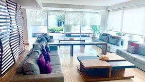 Una sala de estar moderna con un sofá, dos mesas de centro y un ventanal con persianas.