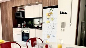 Una cocina moderna con armarios blancos, microondas integrado y refrigerador con exhibición de frutas.