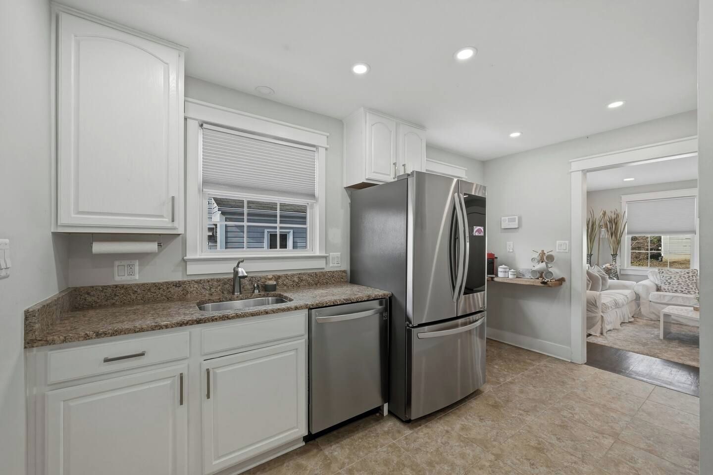 Una cocina moderna con muebles blancos, un refrigerador de acero inoxidable y una encimera de granito.