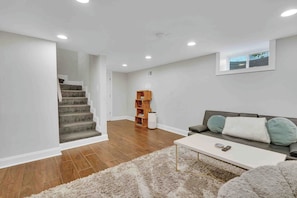A living room with a staircase, a white couch, a coffee table, and a bookshelf.