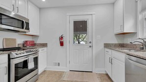 A modern kitchen with white cabinetry, a stainless steel oven, a microwave, and a red toaster. - The Cottage on Royal - Historic Leesburg Home (Leesburg)