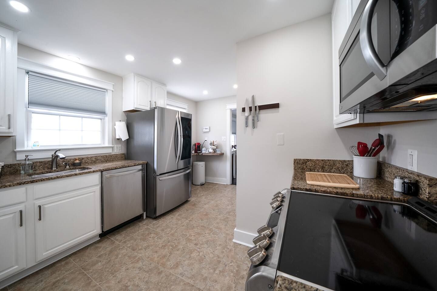 A modern kitchen with white cabinets, a stainless steel refrigerator, a built-in oven, and a granite countertop.
