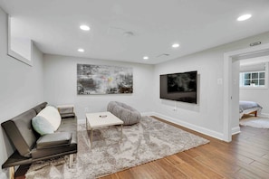 A modern living room with a grey sofa, a white coffee table, a grey bean bag, and a large abstract painting on the wall.