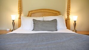 Een bed met een houten hoofdbord, witte lakens en twee bedlampjes.