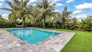 Una piscina rectangular amb un videtrajat, envoltada per un jardí ben cuidat i palmeres.