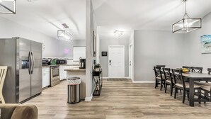 Cuina moderna amb electrodomèstics d'acer inoxidable, zona de menjador amb caires de fusta i un passadís que condueix a una porta.