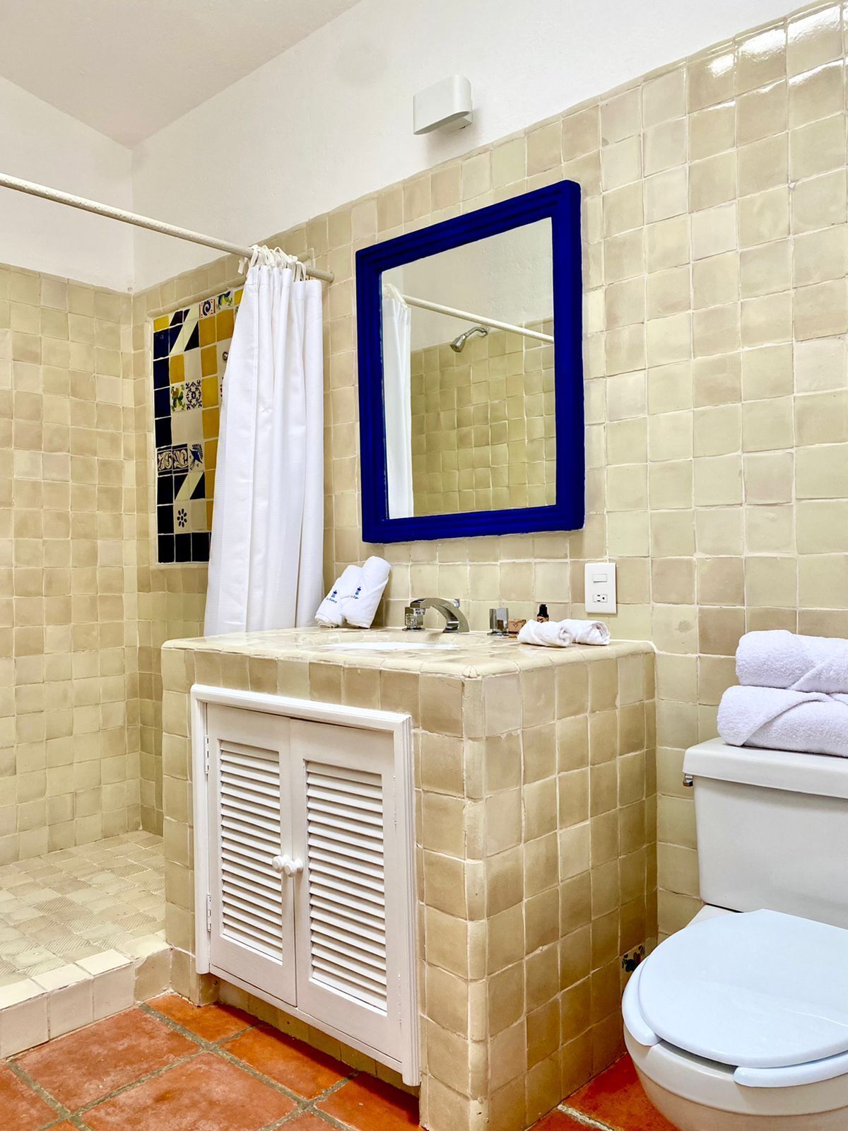 A bathroom with beige tiled walls, a white toilet, a sink with a mirror above it, and a shower area.