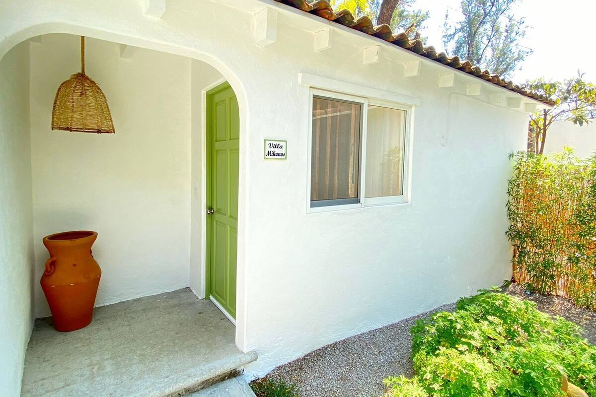 Un edificio bianco con una porta verde, una finestra e un cartello che riporta “Villa Mikonos”.