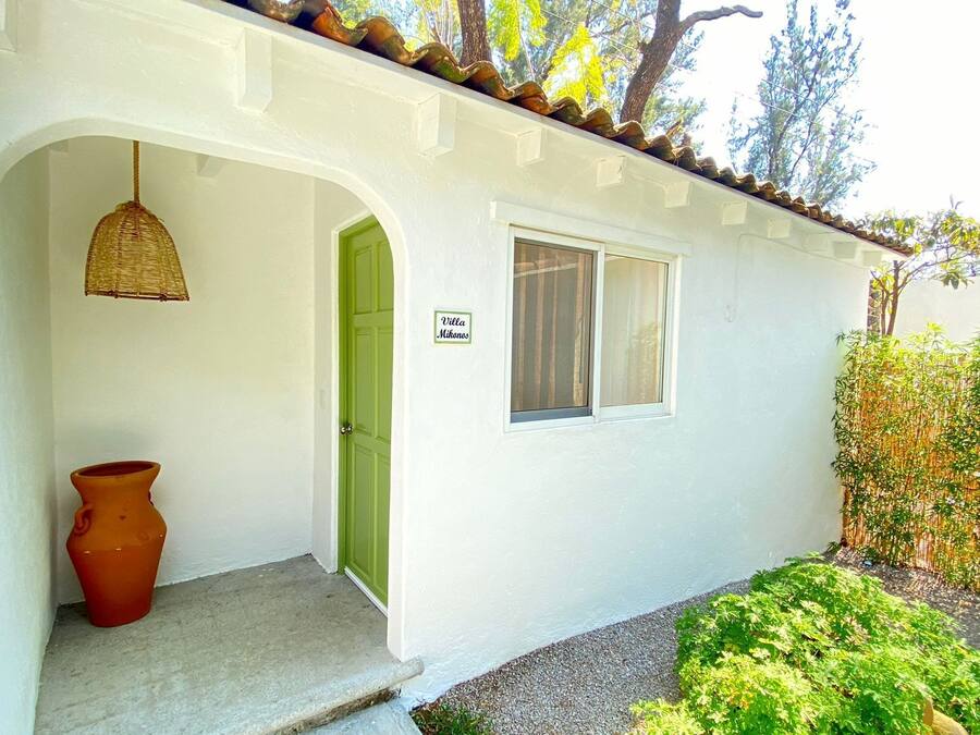 Un edificio blanco con una puerta verde, una ventana y un letrero que dice "Villa Mikonos".