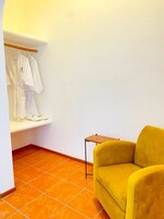 Una habitación con una silla amarilla, un banco con toallas blancas y suelo de baldosas naranjas.