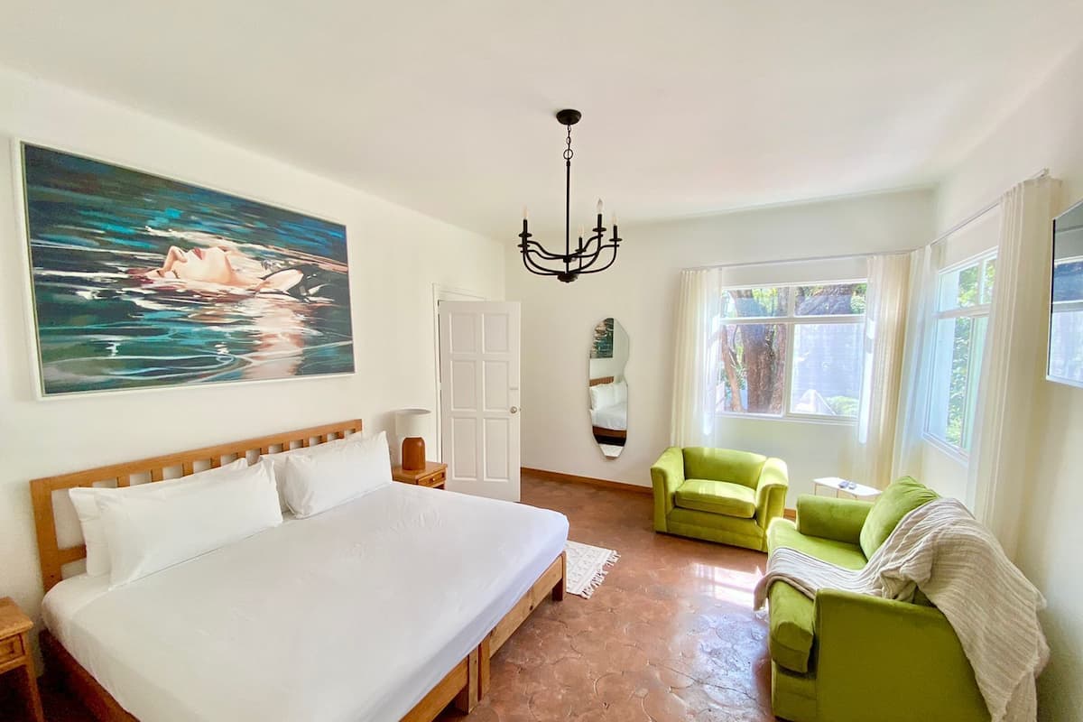 Una camera da letto con un letto grande, una poltrona verde, uno specchio e un quadro raffigurante una scena acquatica.