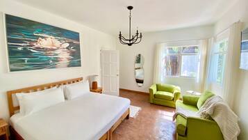 Un dormitorio con una cama grande, un sillón verde, un espejo y un cuadro de una escena acuática.