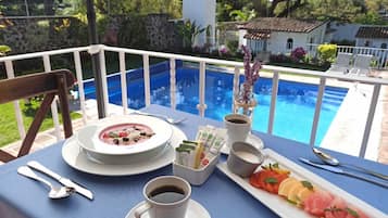 Una mesa de comedor con un tazón de sopa, una taza de café, un plato de fruta y un pequeño jarrón con flores.