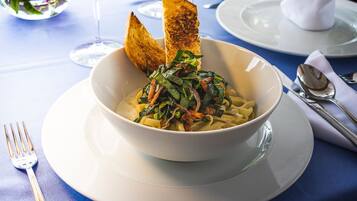 Un plato de pasta con vegetales y tocino, servido en un plato blanco con un tenedor al lado.