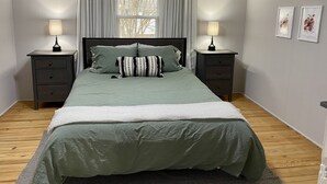 A bedroom with a bed, two nightstands, a window with curtains, and framed pictures on the wall. - Quaint 2 bed 1 bath cottage style home (Kernersville)