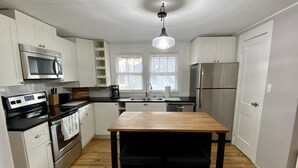 A modern kitchen with white cabinets, stainless steel appliances, a wooden table, and black chairs. - Quaint 2 bed 1 bath cottage style home (Kernersville)