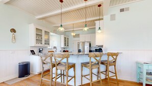 A kitchen with white cabinets, a central island with bar stools, and pendant lighting.