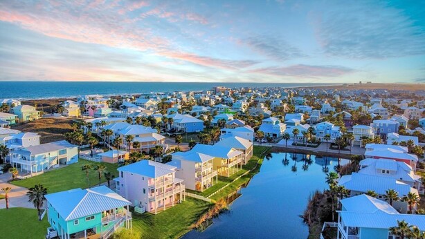 A coastal residential area with houses along a waterway, featuring a mix of single and multi-story buildings, some with balconies.