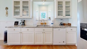 A kitchen with white cabinetry, a built-in dishwasher, and a coffee maker.