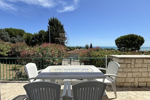 Un patio con mesa y sillas, con vista al mar, árboles y un edificio.