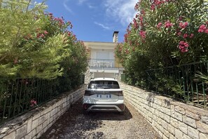 A white SUV parked in a driveway with a stone wall and a building in the background.