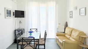 A living room with a glass dining table, a beige sofa, a TV mounted on the wall, and a window with sheer curtains. - N122 - Numana, delightful single villa with garden (Numana)