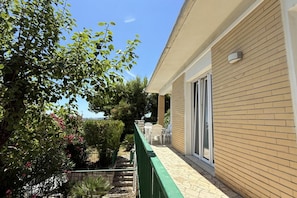A building with a brick exterior, a green metal railing, and a patio area with outdoor furniture.