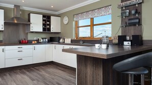 A modern kitchen with white cabinets, a wooden countertop, a stainless steel range hood, and a window with a view.