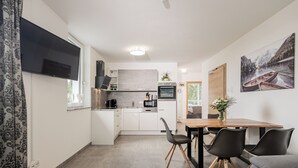 A modern kitchen with a flat-screen TV, wooden flooring, and a dining area with black chairs and a wooden table. - Exclusive apartment with mountain views in a ski paradise (Mauterndorf)