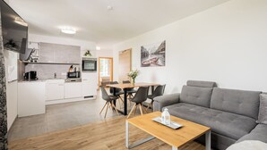 A modern living room with a grey sofa, a wooden coffee table, and a dining area with a wooden table and chairs. - Exclusive apartment with mountain views in a ski paradise (Mauterndorf)