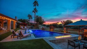 A swimming pool with lounge chairs and a patio area, surrounded by palm trees and a sunset view.