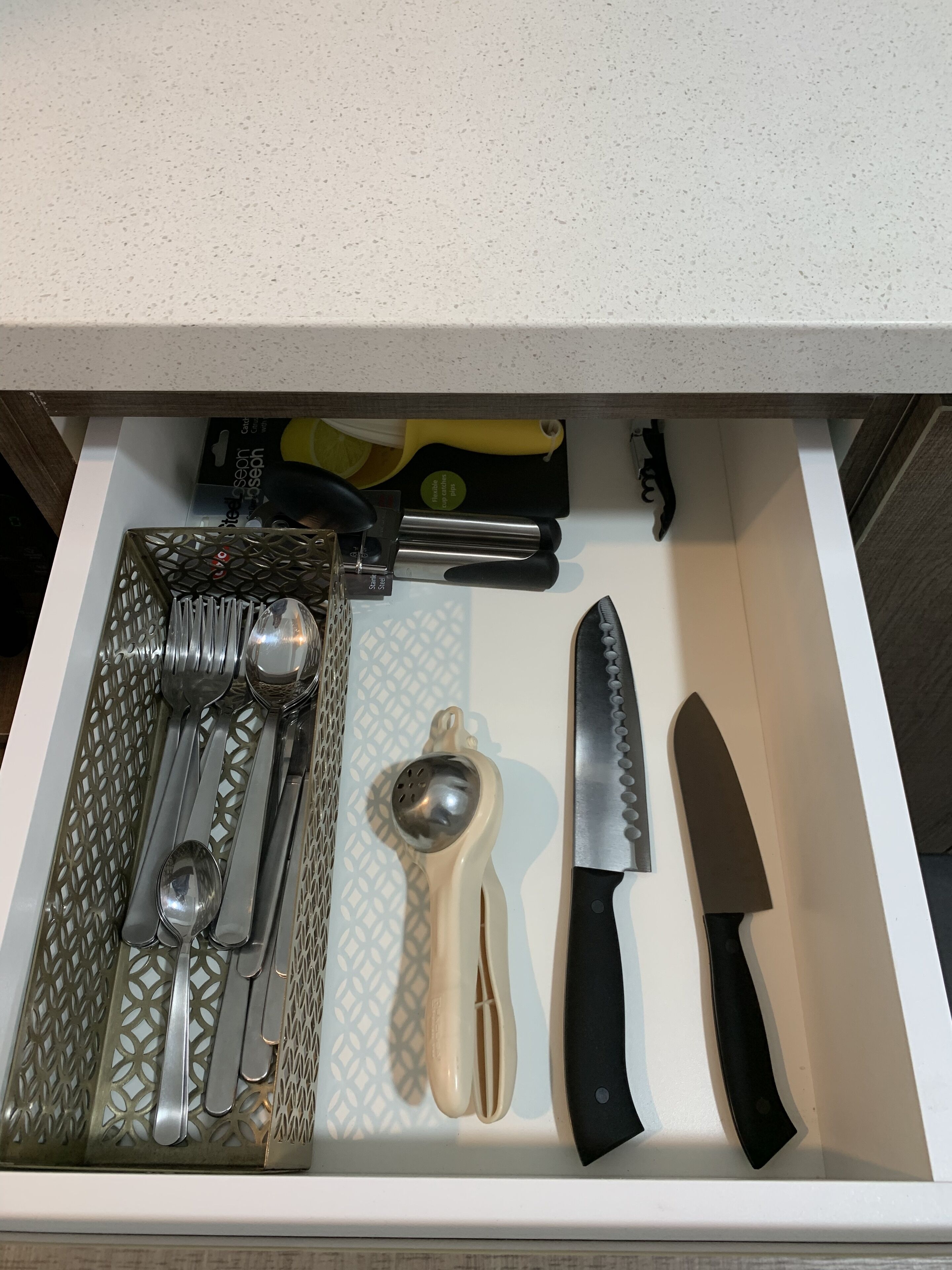 A drawer containing various kitchen utensils including a grater, a knife, and a spoon set.