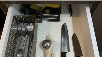 A drawer containing various kitchen utensils including a grater, a knife, and a spoon set.