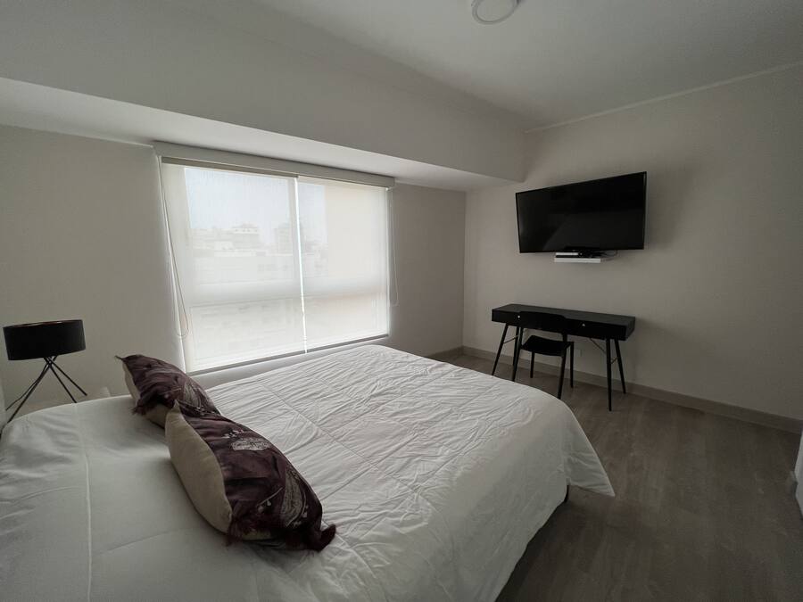 Un dormitorio con cama, escritorio, silla y televisor.