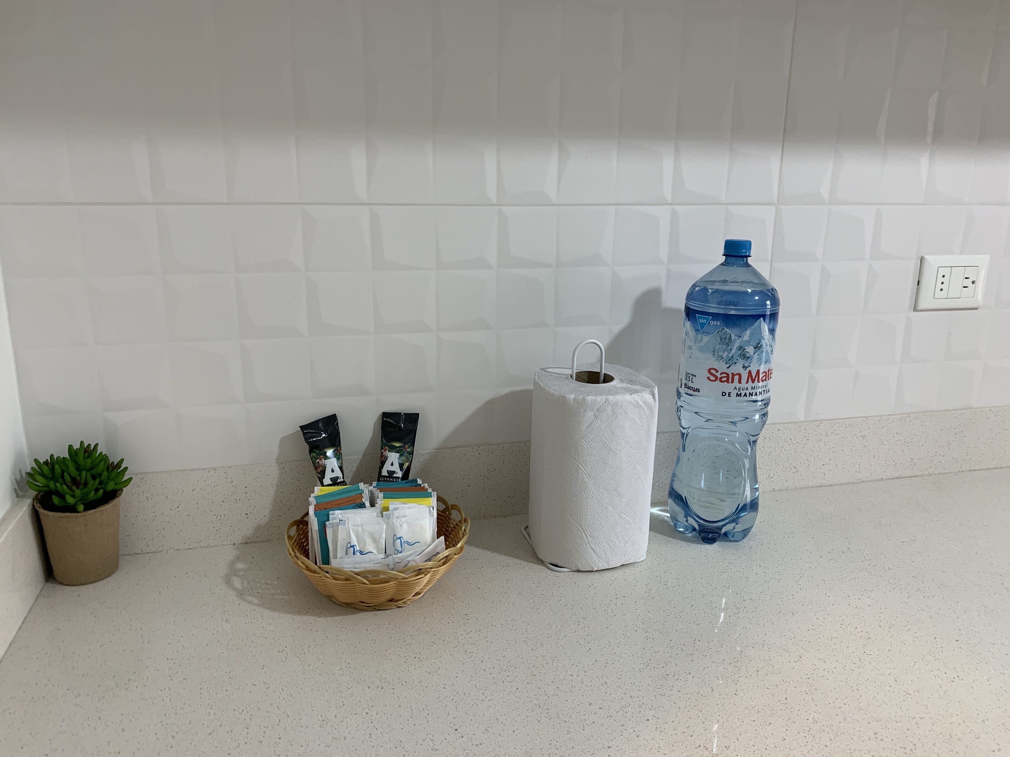 Uma bancada de cozinha com uma garrafa de água, um cesto de produtos de higiene e um rolo de papel toalha.