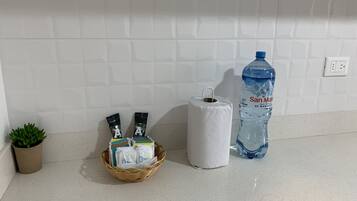 Uma bancada de cozinha com uma garrafa de água, um cesto de produtos de higiene e um rolo de papel toalha.