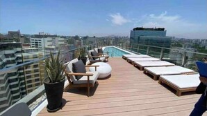 Une terrasse sur le toit avec des chaises longues, une petite piscine et une vue sur la ville.