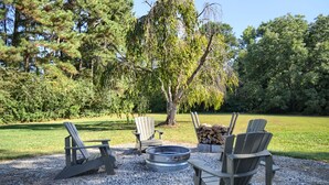 An outdoor seating area with Adirondack chairs and a circular fire pit surrounded by gravel. - Bee Humble Cottage w/in 20mins to Public Beaches (Gloucester)