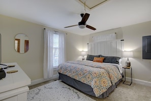 Een slaapkamer met een bed, een plafondventilator, een nachtkastje met een lamp, een dressoir en een spiegel.